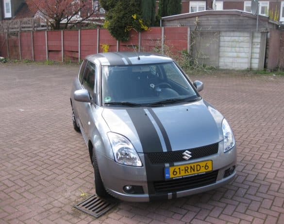 Grijze Suzuki Swift met zwarte rally-striping over de motorkap